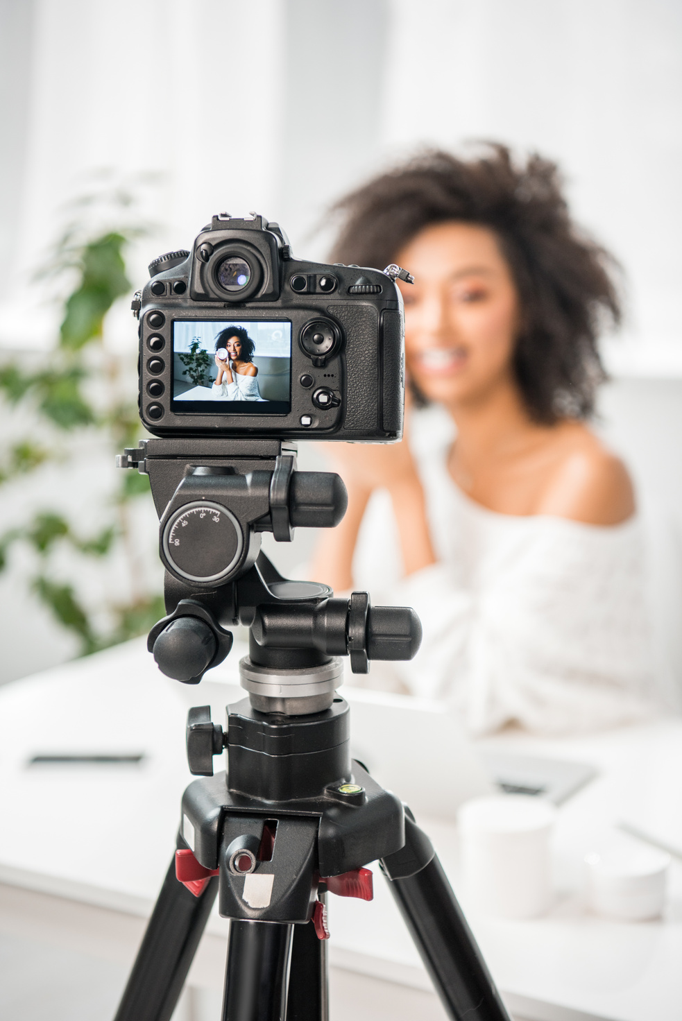 selective focus of digital camera with young african american influencer in braces holding container with cosmetic cream on display